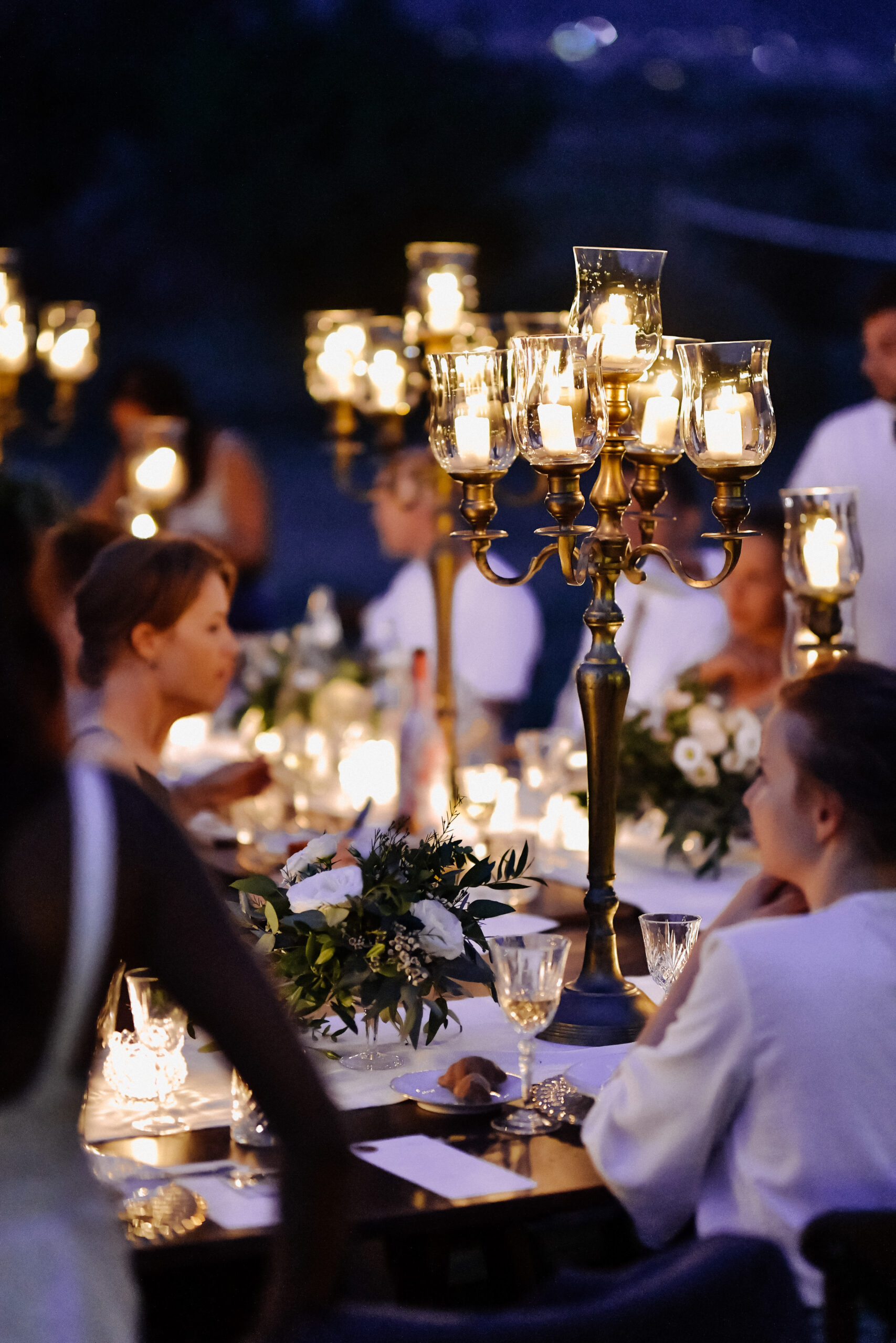 Decorated tables with floral composition and old fashioned candlesticks and guests in the celebration evening